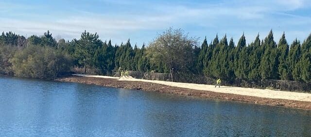 Man walks along compacted path beside detention pond surrounded by trees under a blue sky