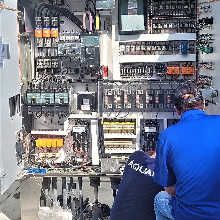 AQUALIS employees looking into a lift station control panel
