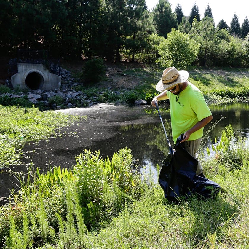 AQUALIS employee picking up trash by a pond
