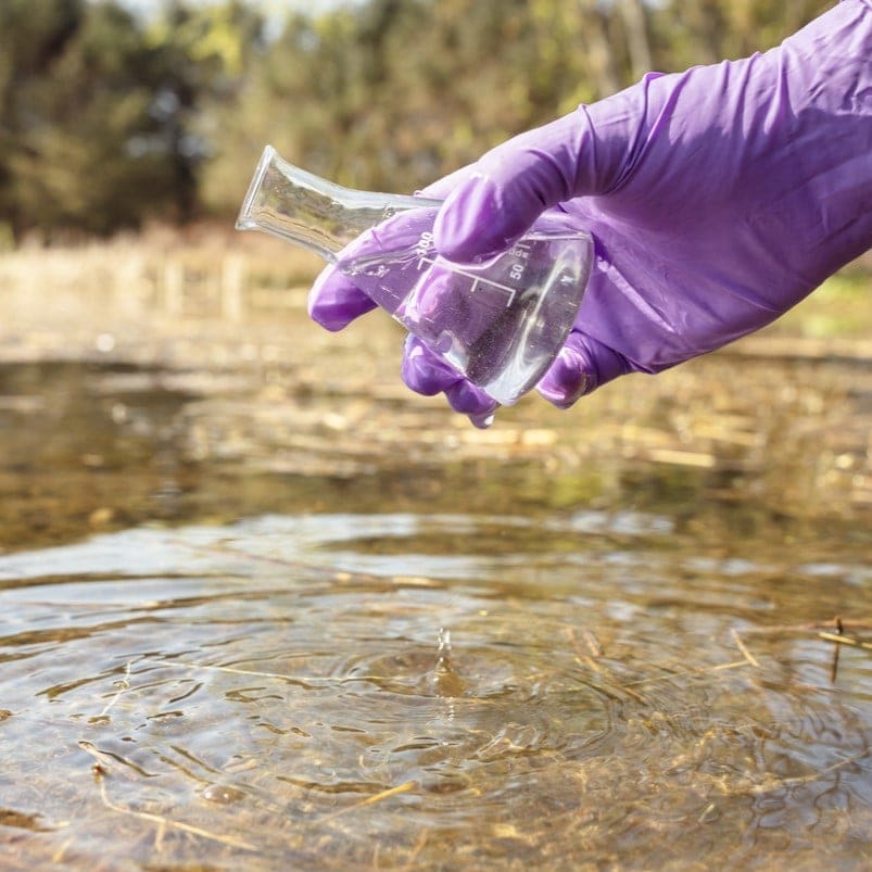 person with glove filling a beaker with pond water