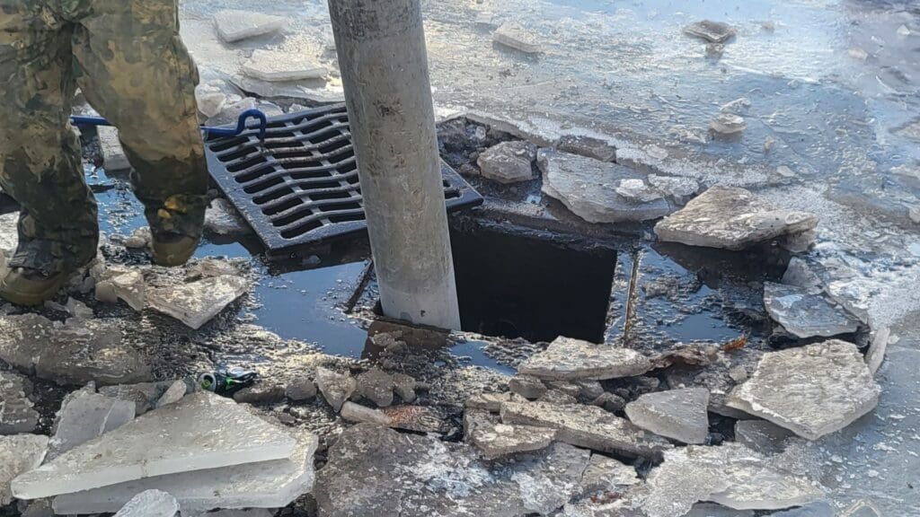 AQUALIS employee opening up a sewer grate around ice