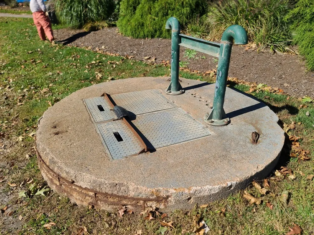 A closeup of a sewer lift with green, rusty, metal pipes sticking up out of one end of it.
