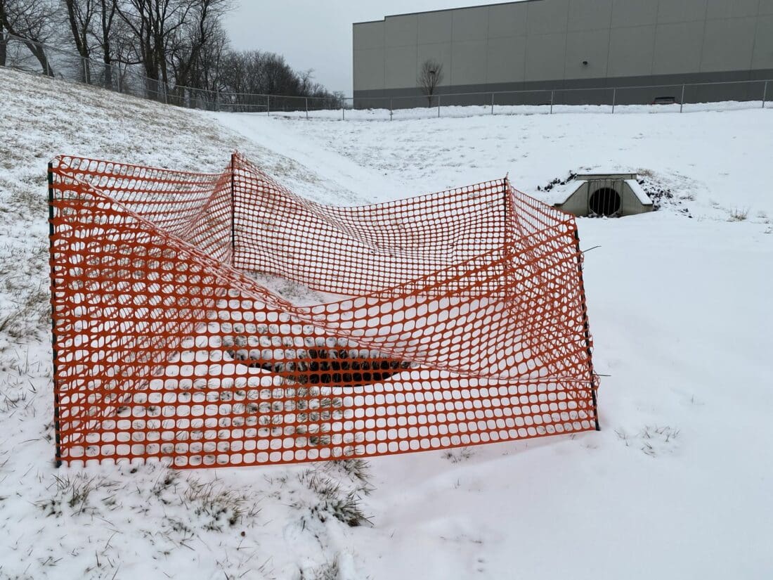 sinkhole in the snow being guarded off by orange fencing