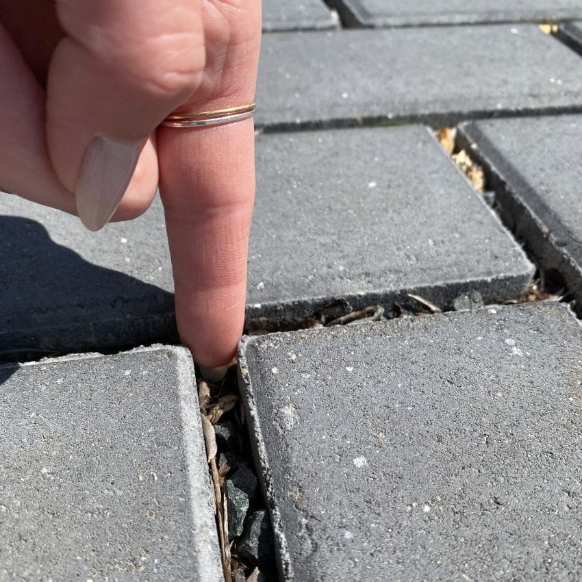 Person's finger between pavers to determine levels of debris